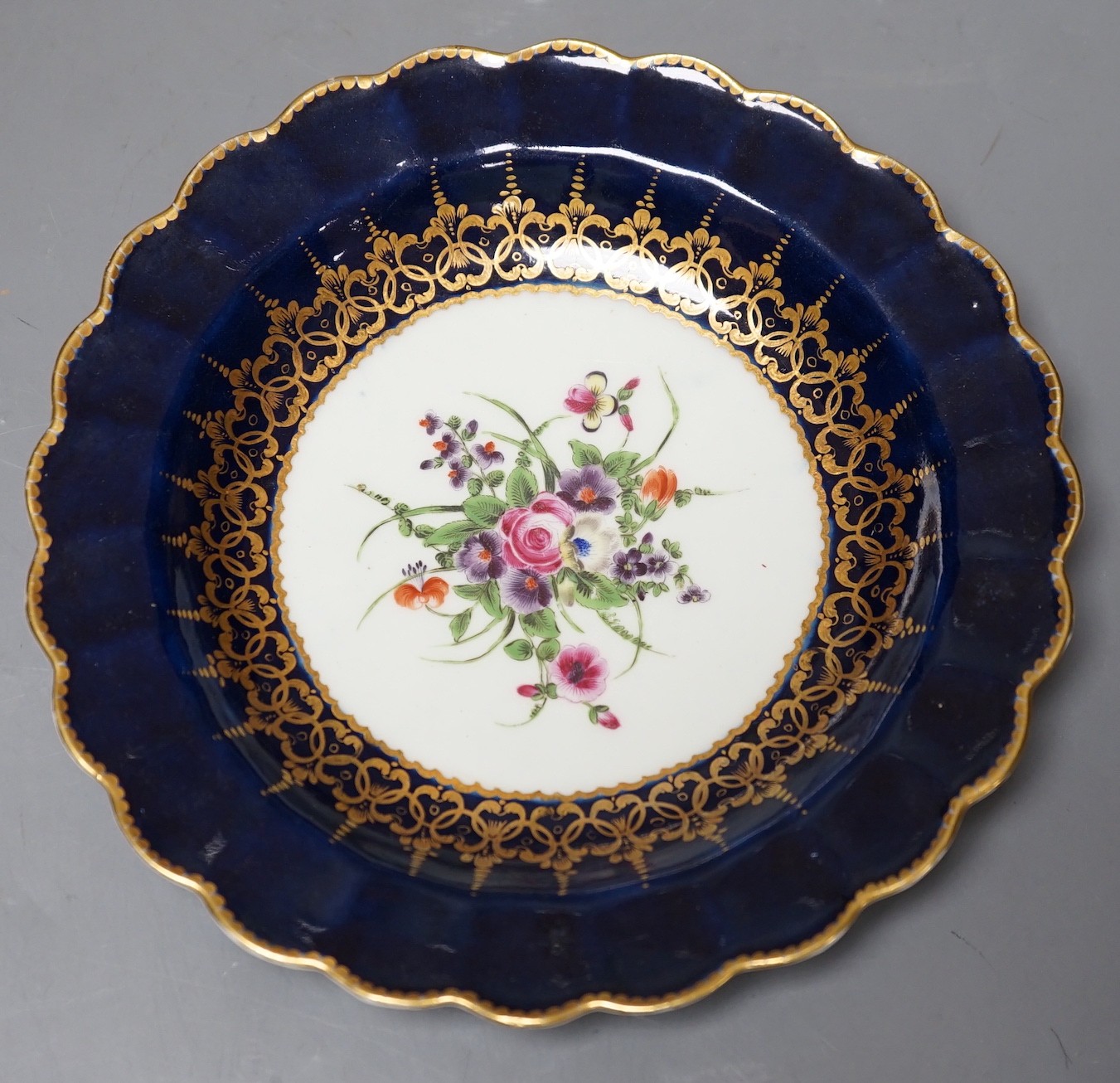 A Worcester plate with wet blue border painted with a bouquet of flowers surrounded by an elaborate gilt inner border, 19 cm diameter